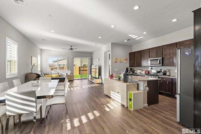 kitchen featuring a breakfast bar, backsplash, dark wood-type flooring, a center island with sink, and stainless steel appliances