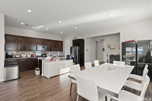 kitchen with a kitchen island with sink, tasteful backsplash, dark brown cabinets, a kitchen bar, and stainless steel appliances