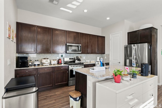 kitchen featuring dark brown cabinets, a kitchen island, dark wood-type flooring, and appliances with stainless steel finishes