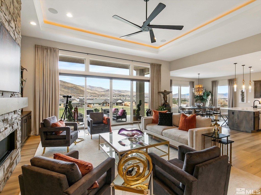 living room with ceiling fan, a stone fireplace, a mountain view, light hardwood / wood-style floors, and a tray ceiling