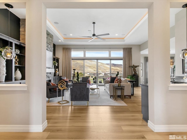 living room featuring a mountain view, a tray ceiling, light hardwood / wood-style flooring, and ceiling fan