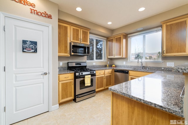 kitchen with stone counters, appliances with stainless steel finishes, kitchen peninsula, and sink