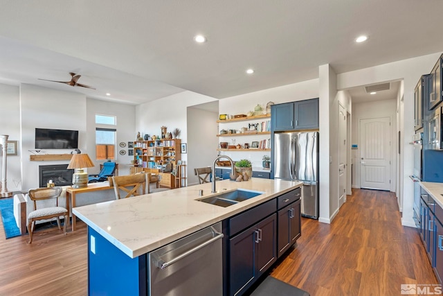 kitchen featuring appliances with stainless steel finishes, light stone counters, dark wood-type flooring, sink, and an island with sink