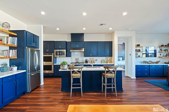 kitchen with blue cabinetry, stainless steel appliances, dark hardwood / wood-style floors, an island with sink, and a breakfast bar area