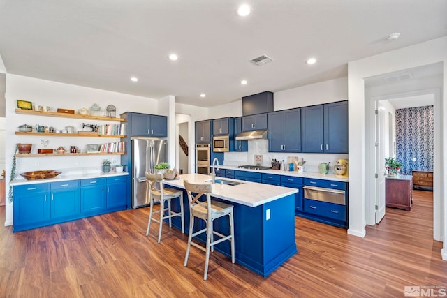 kitchen featuring a kitchen bar, blue cabinetry, an island with sink, appliances with stainless steel finishes, and dark hardwood / wood-style flooring