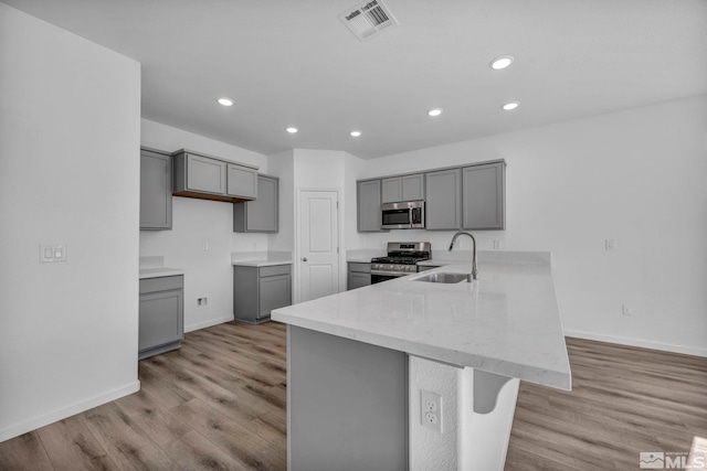 kitchen with kitchen peninsula, appliances with stainless steel finishes, gray cabinetry, sink, and light hardwood / wood-style floors