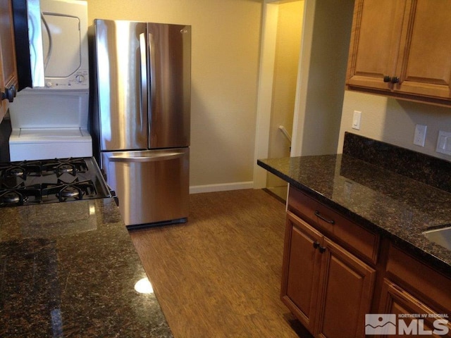 kitchen with stacked washing maching and dryer, stainless steel fridge, light hardwood / wood-style floors, dark stone counters, and range