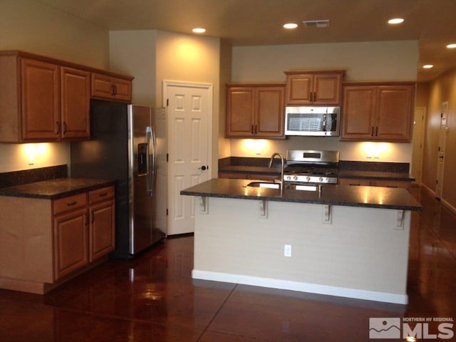 kitchen with sink, dark stone countertops, an island with sink, a kitchen bar, and stainless steel appliances