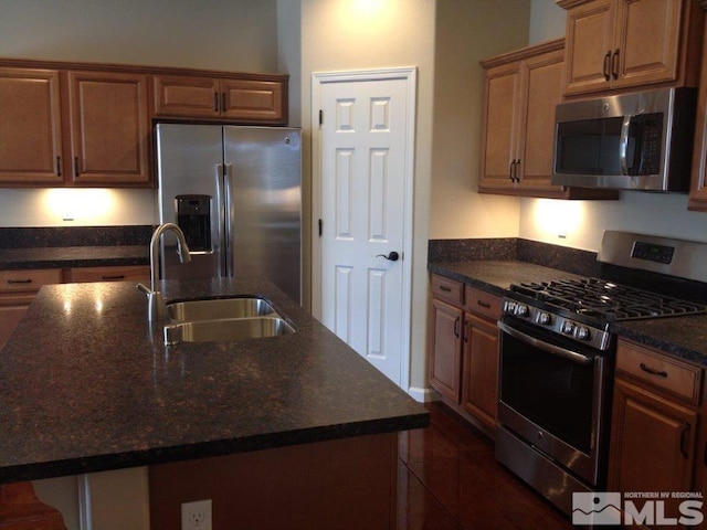 kitchen with sink, stainless steel appliances, dark stone counters, and an island with sink