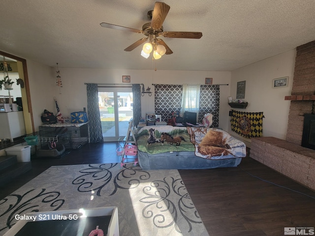 living room featuring ceiling fan, dark hardwood / wood-style flooring, a textured ceiling, and a brick fireplace