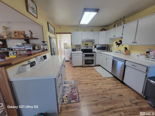 kitchen with appliances with stainless steel finishes, light hardwood / wood-style flooring, white cabinets, washer / dryer, and tile counters