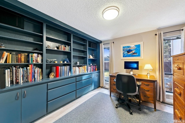 office space featuring built in features, light hardwood / wood-style floors, and a textured ceiling