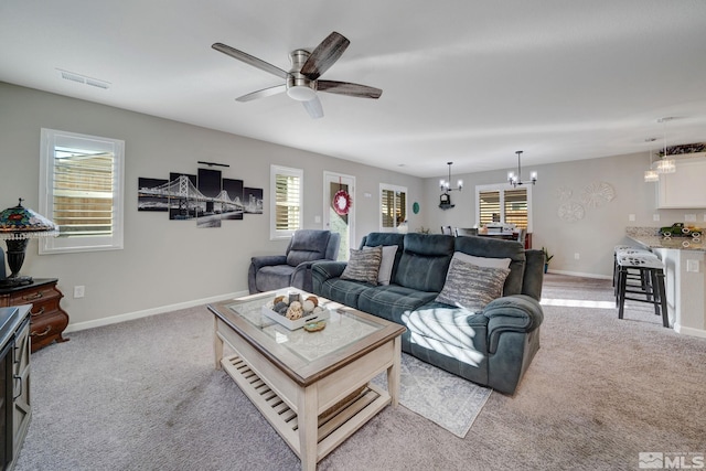 living room featuring light carpet, plenty of natural light, and ceiling fan with notable chandelier