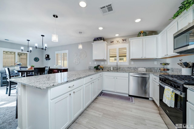 kitchen with sink, stainless steel appliances, kitchen peninsula, decorative light fixtures, and white cabinets