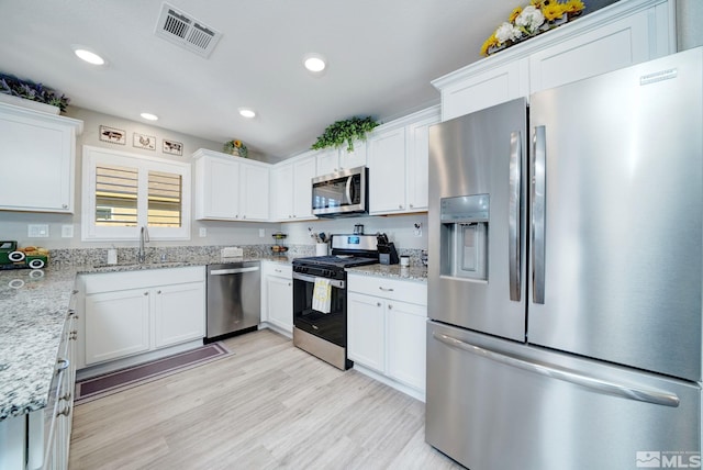 kitchen with sink, light stone countertops, appliances with stainless steel finishes, light hardwood / wood-style floors, and white cabinetry