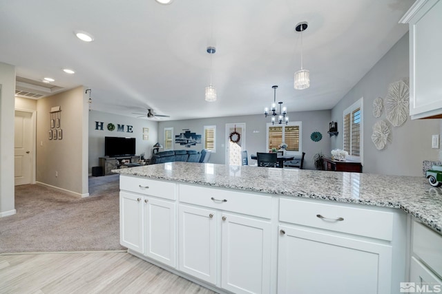 kitchen with ceiling fan, white cabinets, light stone counters, and decorative light fixtures