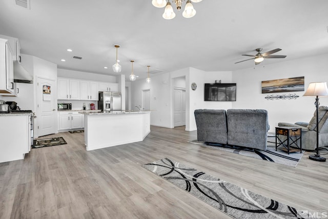 kitchen with pendant lighting, stainless steel fridge with ice dispenser, an island with sink, range hood, and white cabinetry