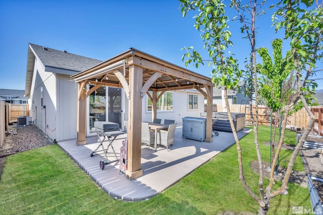 rear view of property featuring a gazebo, central AC unit, a patio area, a yard, and a hot tub