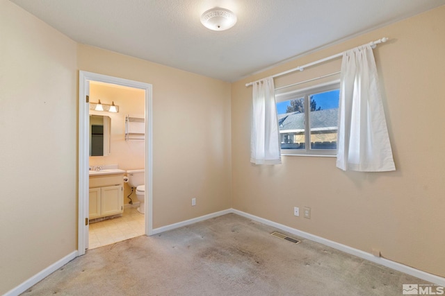 unfurnished bedroom featuring sink, light carpet, and ensuite bath