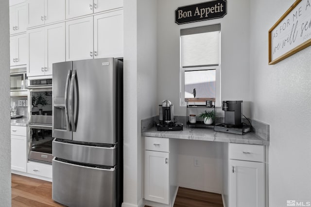 kitchen with appliances with stainless steel finishes, built in desk, light hardwood / wood-style floors, and white cabinetry