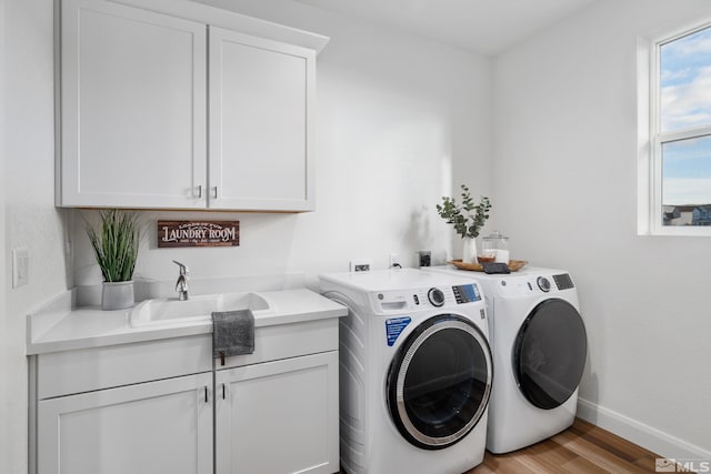 clothes washing area featuring washer and clothes dryer, cabinets, light wood-type flooring, and sink