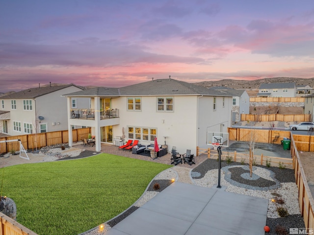 back house at dusk with an outdoor living space, a yard, a balcony, and a patio