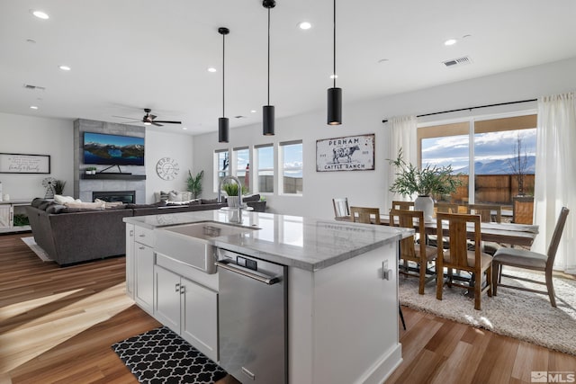 kitchen featuring white cabinetry, ceiling fan, light stone countertops, sink, and a center island with sink