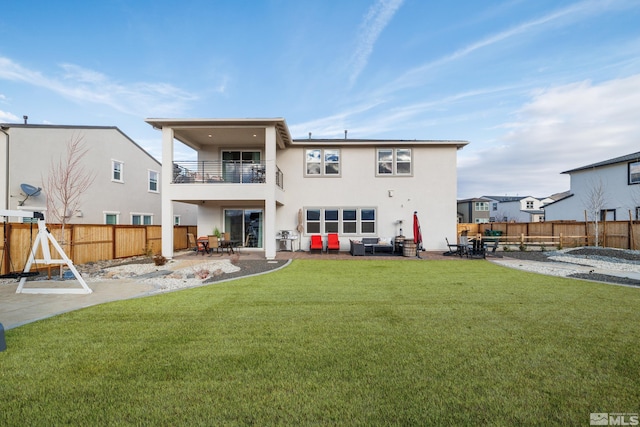 rear view of property with a lawn, a balcony, and a patio