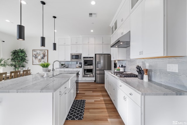 kitchen featuring backsplash, a kitchen island with sink, white cabinets, hanging light fixtures, and stainless steel appliances