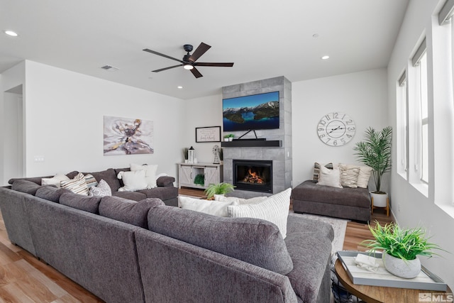 living room featuring a tile fireplace, ceiling fan, and light hardwood / wood-style floors