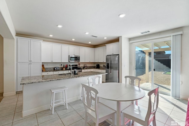 kitchen with light stone countertops, a kitchen breakfast bar, stainless steel appliances, light tile patterned floors, and white cabinetry