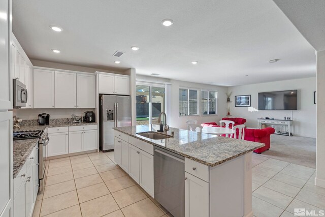 kitchen featuring light stone counters, stainless steel appliances, sink, white cabinetry, and an island with sink