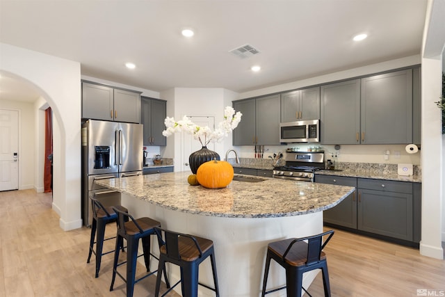 kitchen with gray cabinetry, stainless steel appliances, a center island with sink, and sink