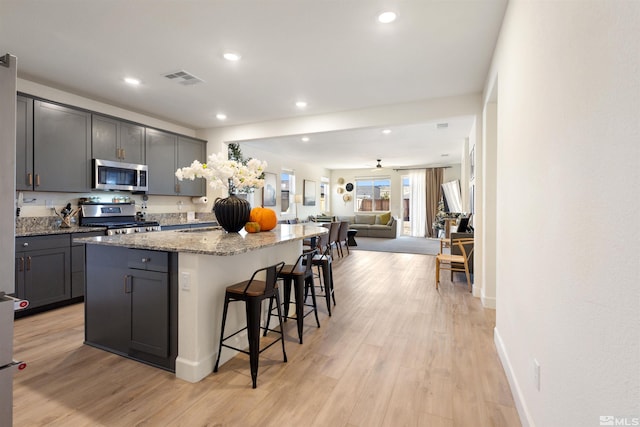 kitchen with a breakfast bar, gray cabinets, stainless steel appliances, and a kitchen island