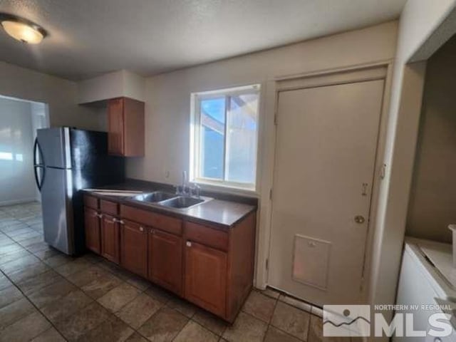 kitchen with brown cabinetry, freestanding refrigerator, a sink, and dark countertops