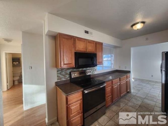 kitchen featuring tasteful backsplash, visible vents, brown cabinetry, dark countertops, and black appliances