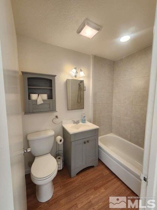 bathroom with a textured ceiling, toilet, wood finished floors, vanity, and a bath