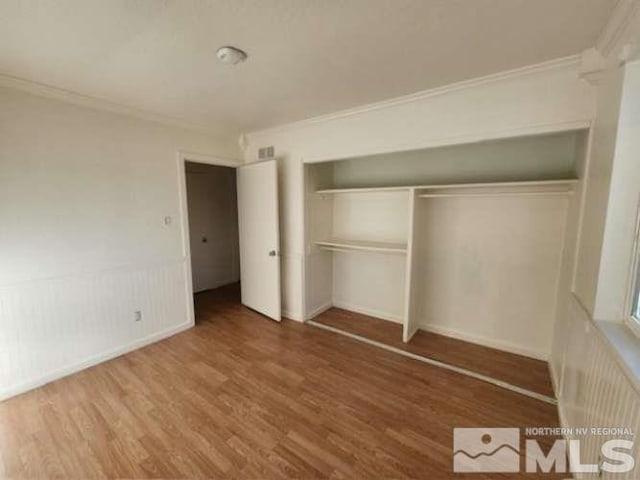 unfurnished bedroom with ornamental molding, a closet, a wainscoted wall, and wood finished floors