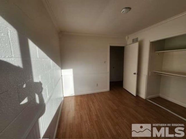 unfurnished bedroom featuring baseboards, a closet, wood finished floors, and crown molding