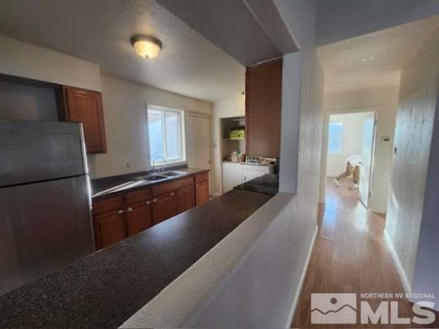 kitchen with a sink, light wood-style floors, freestanding refrigerator, open shelves, and washing machine and clothes dryer