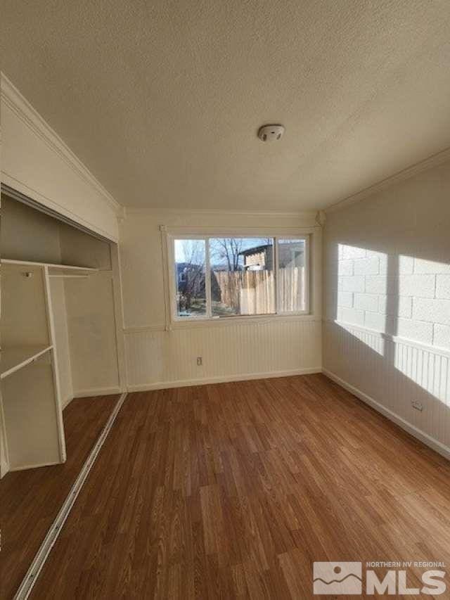 unfurnished bedroom with crown molding, a textured ceiling, a closet, and wood finished floors