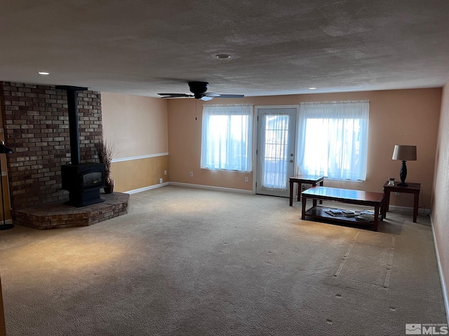 unfurnished living room with a textured ceiling, ceiling fan, a wood stove, and light carpet