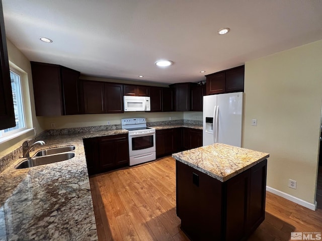 kitchen featuring a center island, light stone countertops, white appliances, and sink