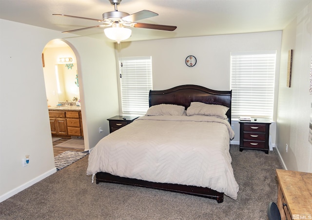 bedroom featuring ceiling fan, ensuite bath, and dark colored carpet