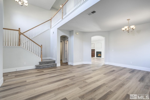 unfurnished living room with a notable chandelier, light wood-type flooring, and a high ceiling