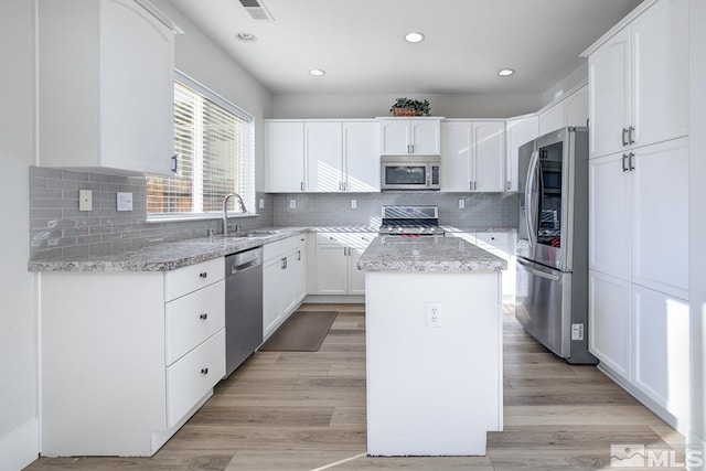 kitchen with white cabinetry, sink, a center island, light stone countertops, and appliances with stainless steel finishes