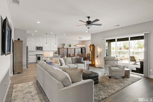 living room with light wood-type flooring and ceiling fan with notable chandelier