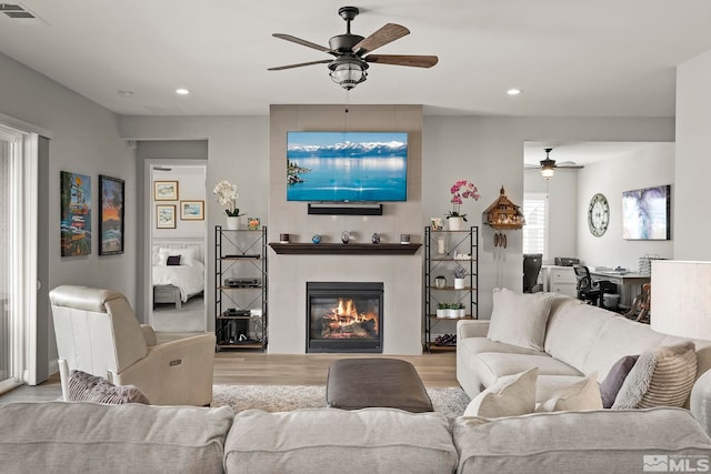 living room with ceiling fan, light hardwood / wood-style floors, and a tiled fireplace