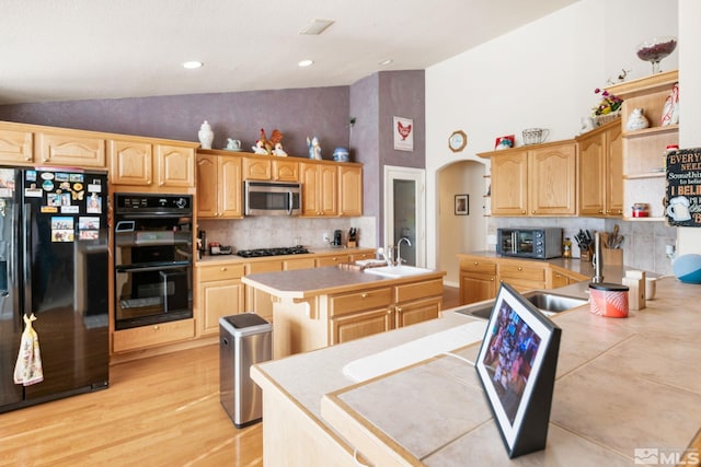 kitchen with tasteful backsplash, sink, black appliances, a center island with sink, and light hardwood / wood-style flooring