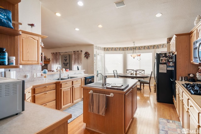 kitchen featuring black appliances, a center island with sink, sink, light wood-type flooring, and decorative light fixtures